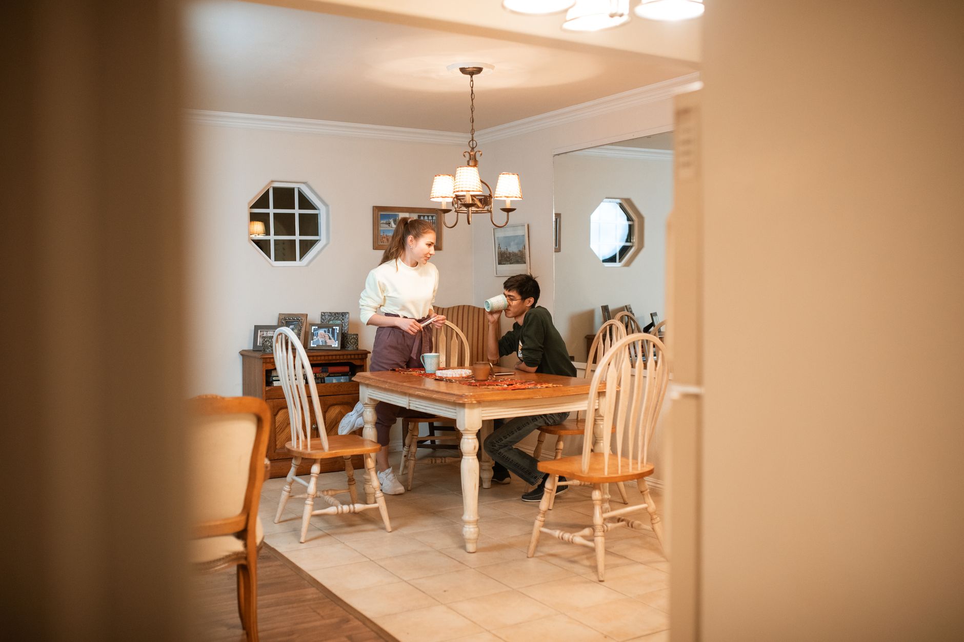 Een vrouw staat bij de eettafel en praat met haar partner, die aan tafel koffie drinkt